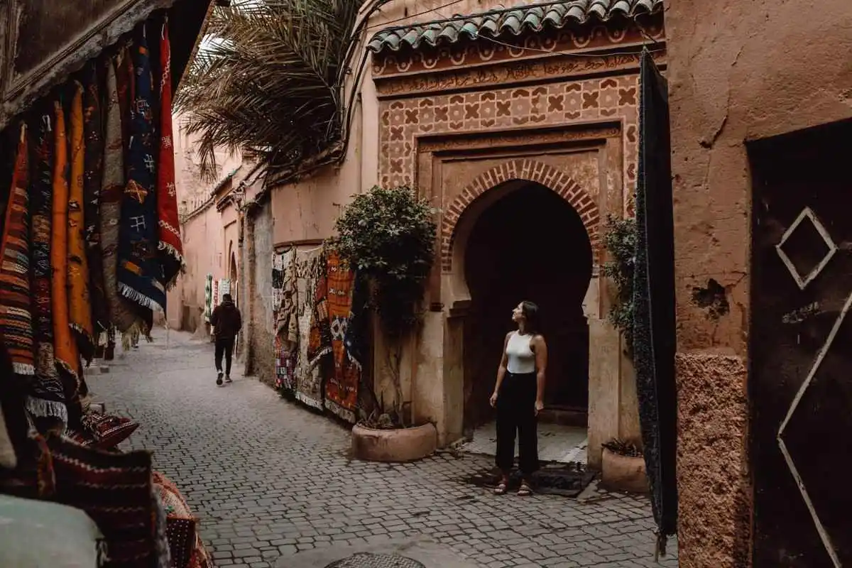 Woman exploring traditional Moroccan medina street lined with colorful carpets and historic arches.