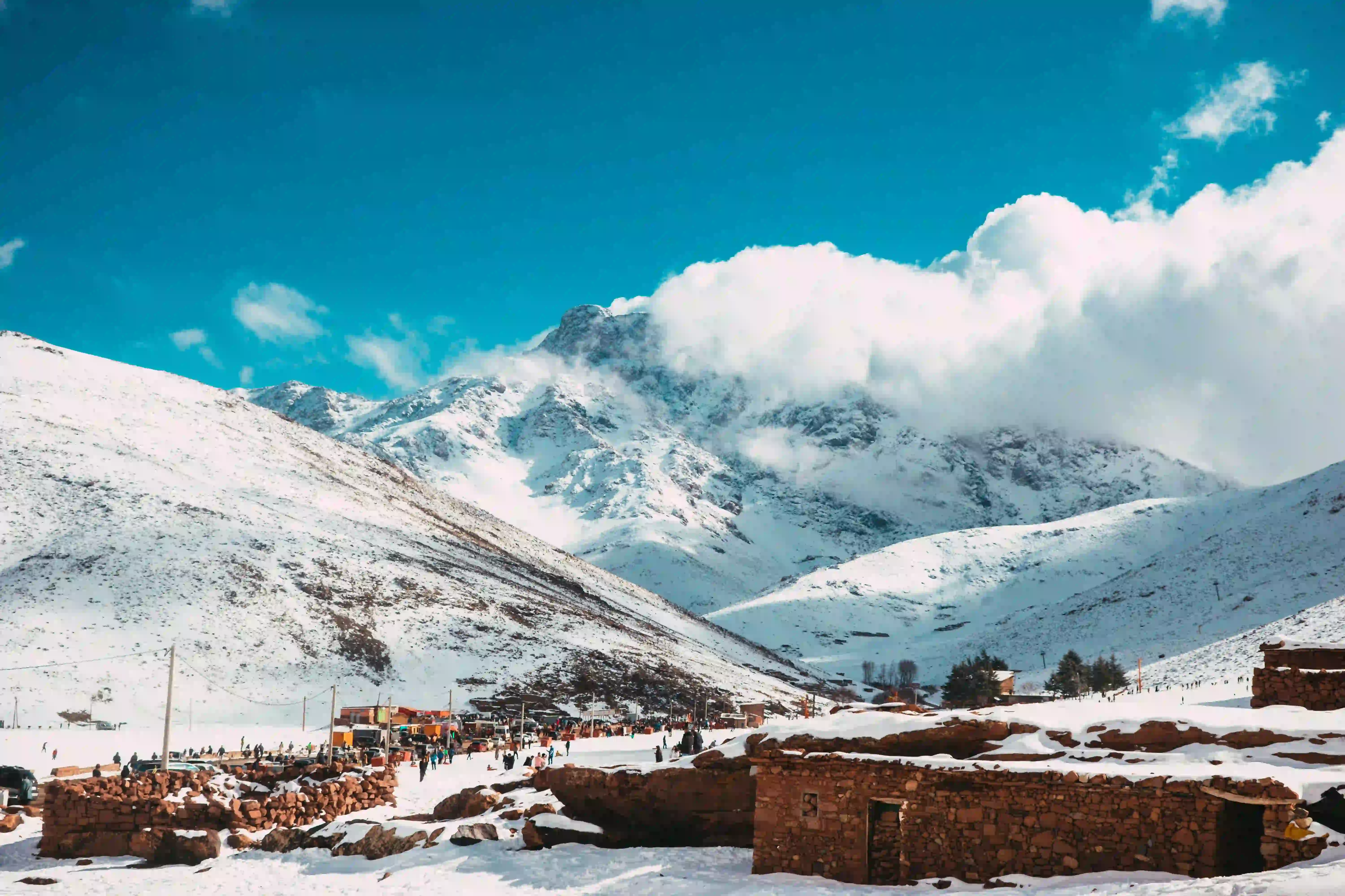 Snow-capped High Atlas mountain peaks rising above red-earth foothills on a Morocco trekking route