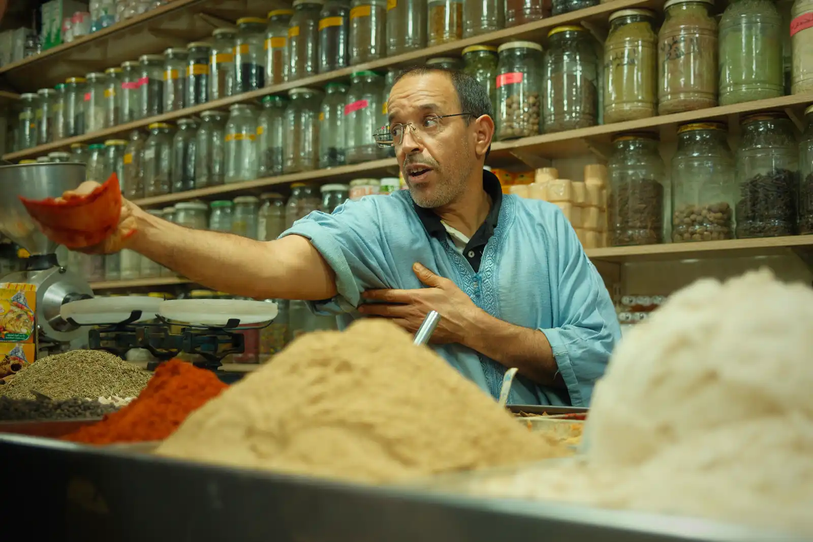 Moroccan spice merchant serving a customer beside colorful mounds of spices in a Marrakech souk